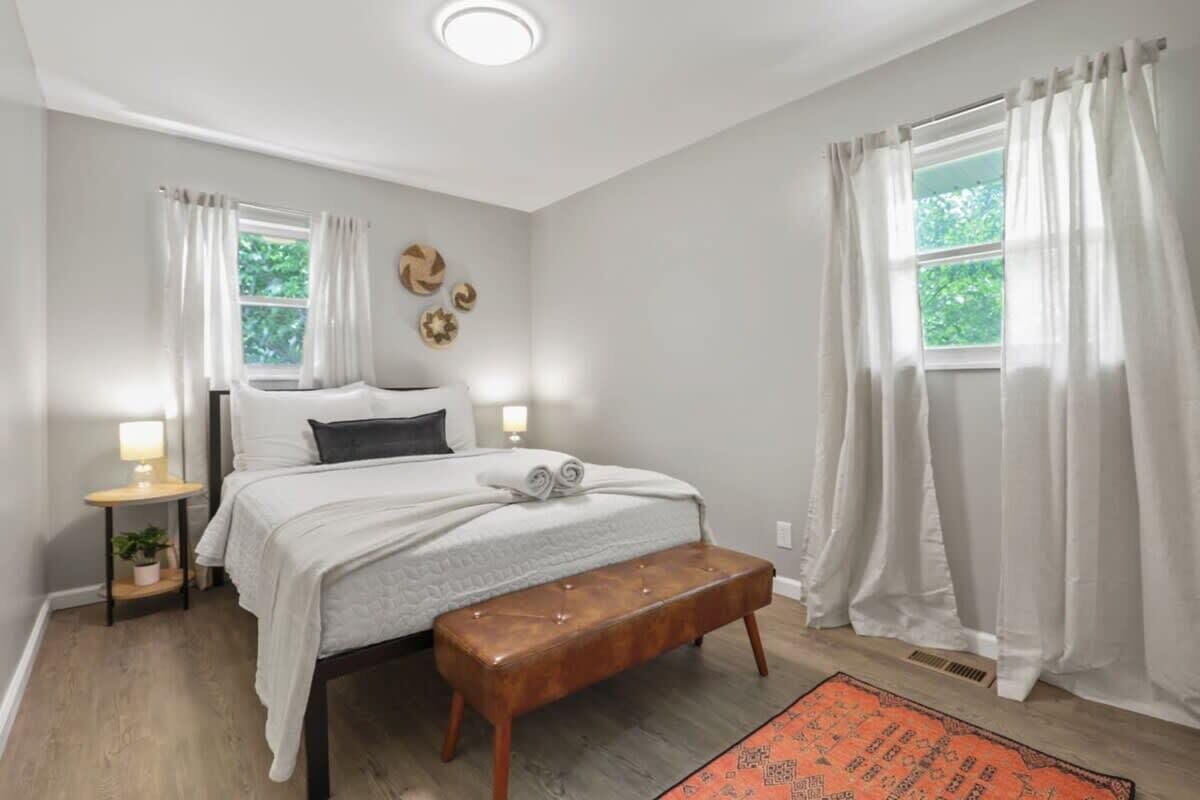 Une chambre à coucher avec un lit, des tables de chevet, un banc et une fenêtre avec des rideaux.