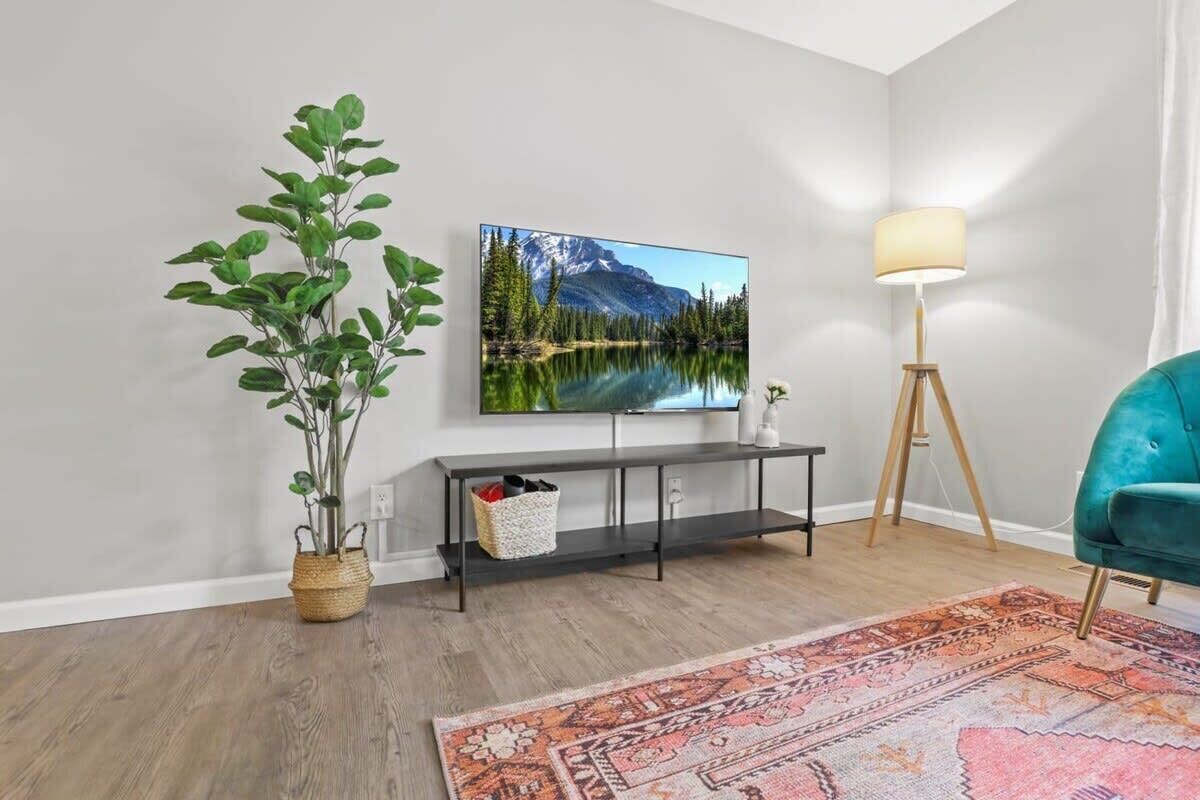 Un salon avec un téléviseur, une plante, une lampe et un fauteuil de couleur turquoise.