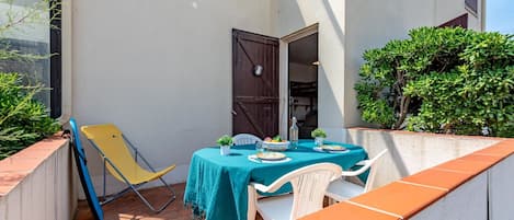 A small outdoor patio with a table set for two, a yellow chair, and a white chair.