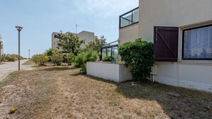 A modern building with a flat roof, large windows, and a well-maintained garden with shrubs and a small tree. - Beautiful apartment for 3 guests with WIFI, TV and terrace (Le Barcarès)