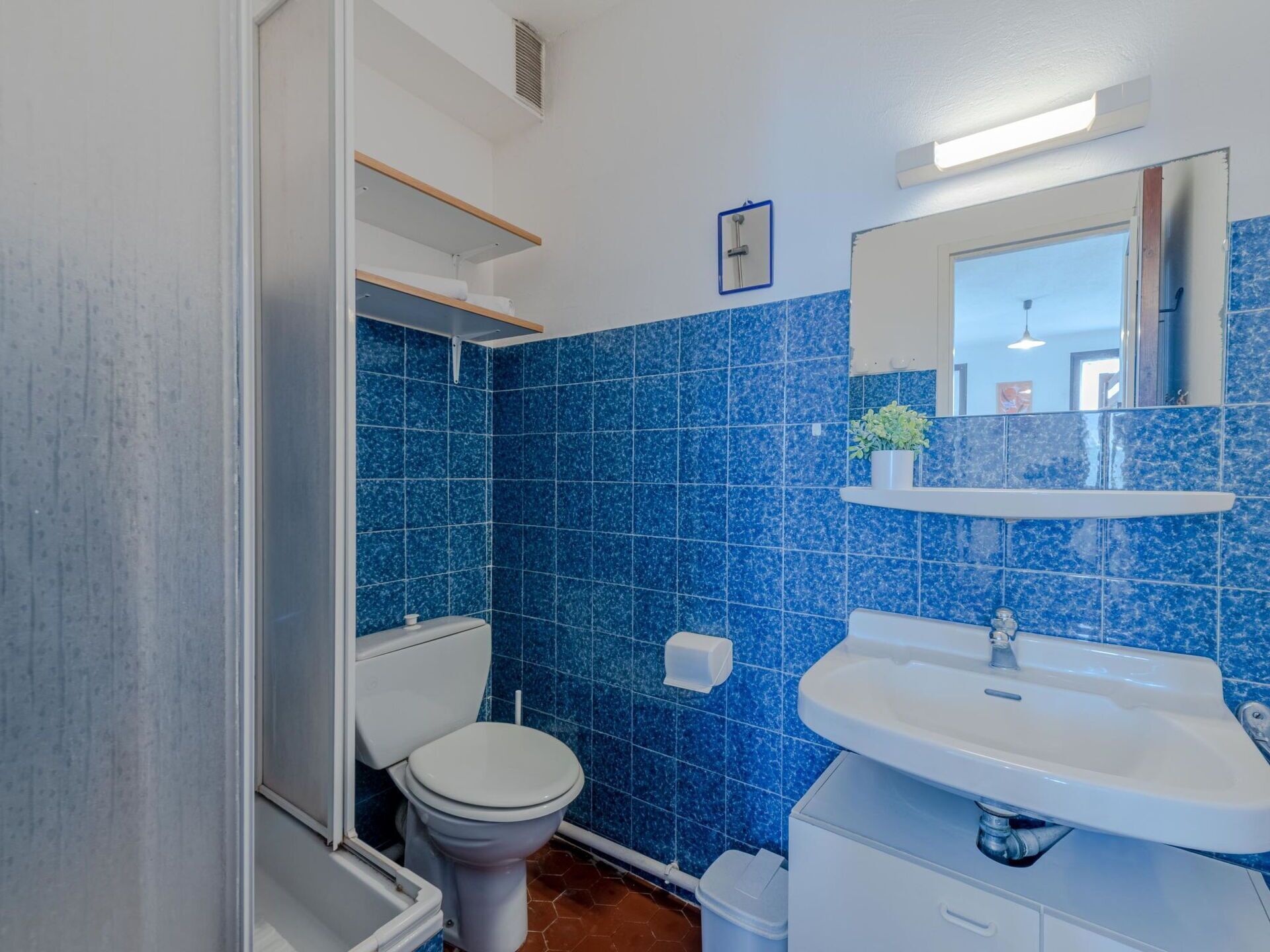 Une salle de bain avec des carreaux bleus, des toilettes blanches, un lavabo blanc et un miroir au-dessus du lavabo.