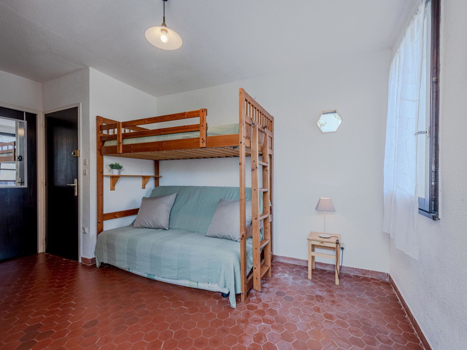 A bunk bed with a wooden frame, a small bedside table, and a lamp.