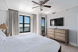 A hotel room with a large bed, a ceiling fan, a TV, a dresser, and a balcony with a view.