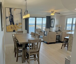 A spacious living area with a wooden dining table, beige sofas, and a view of the ocean.
