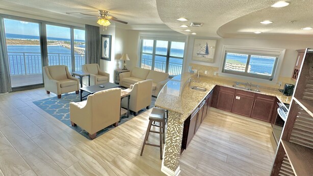 A spacious living area with a large window overlooking the sea, a kitchen with a granite countertop, and a balcony with a view of the ocean.