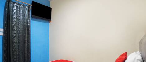 Una habitación con una cama, un televisor en la pared y una cortina.