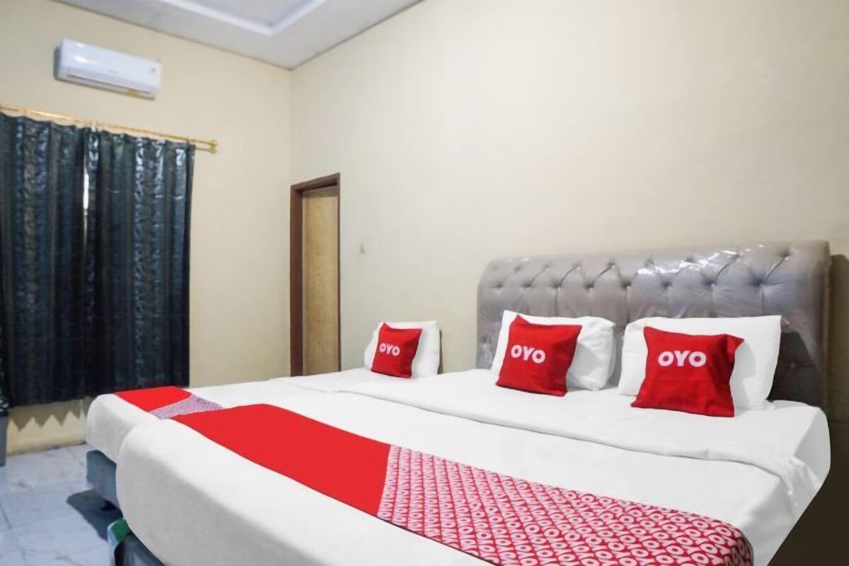 A hotel room with a bed, a red and white patterned bedspread, and three red pillows with the word "OYO" on them.