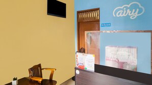 A reception desk with a sign for 'airy' hotel, a wooden chair, a small potted plant, and a wall-mounted screen. - Hotel O Sky Residence Mawar (Medan)
