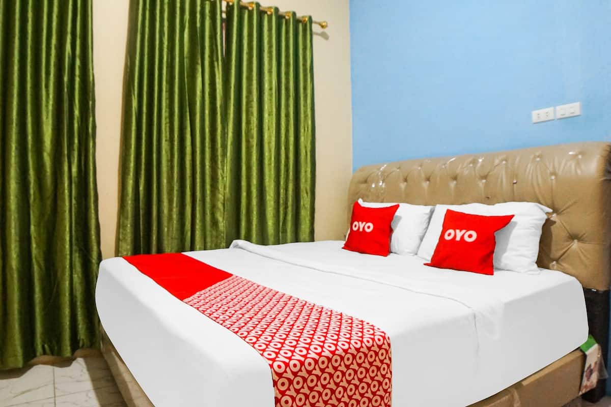A neatly made bed with a red and white patterned bedspread and two red pillows with the word "OYO" on them.