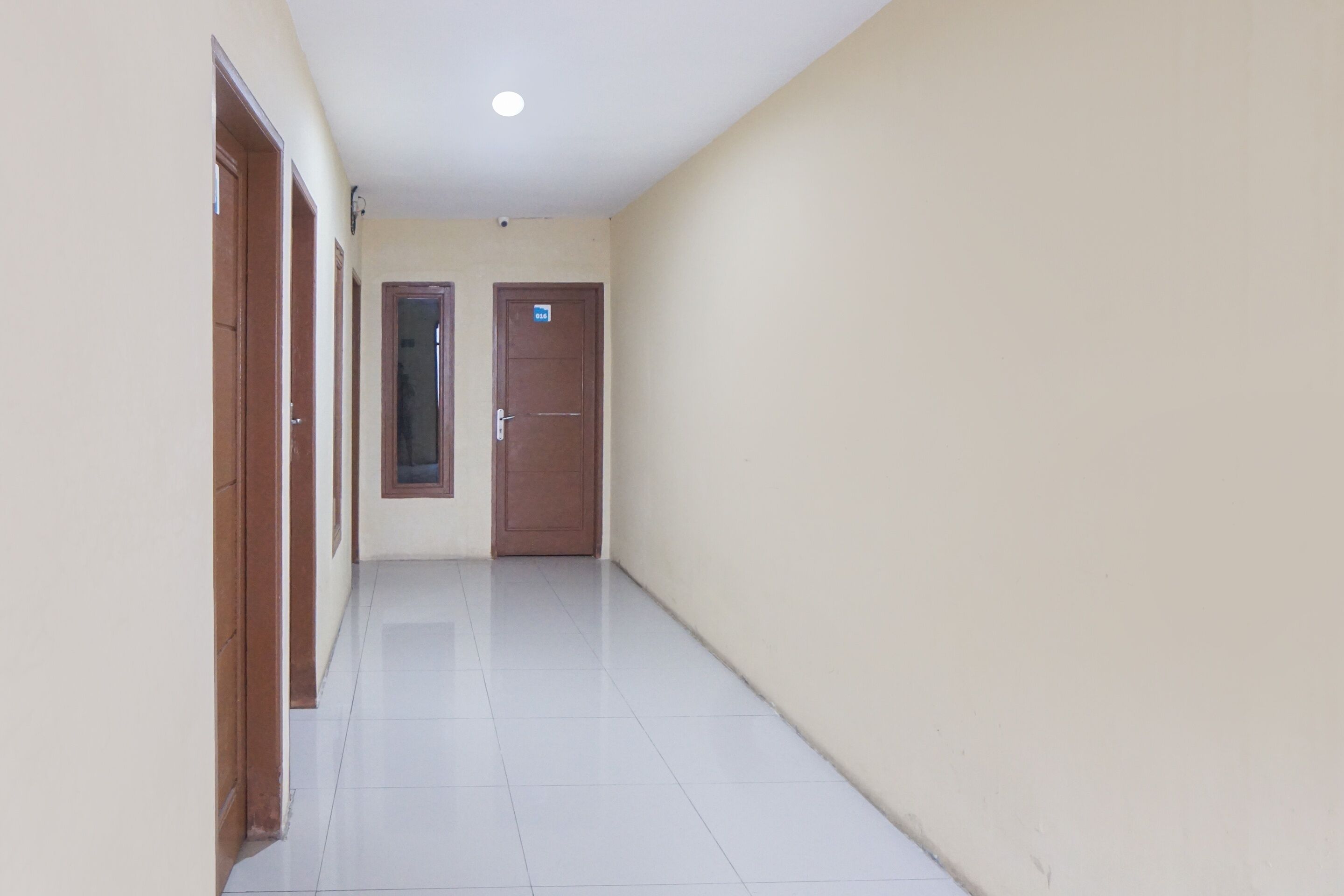 A corridor with a tiled floor, wooden doors, and a plain wall.