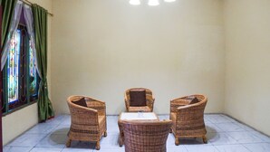 A room with three wicker chairs, a small table, a chandelier, and a window with green curtains. - Hotel O Sky Residence Mawar (Medan)