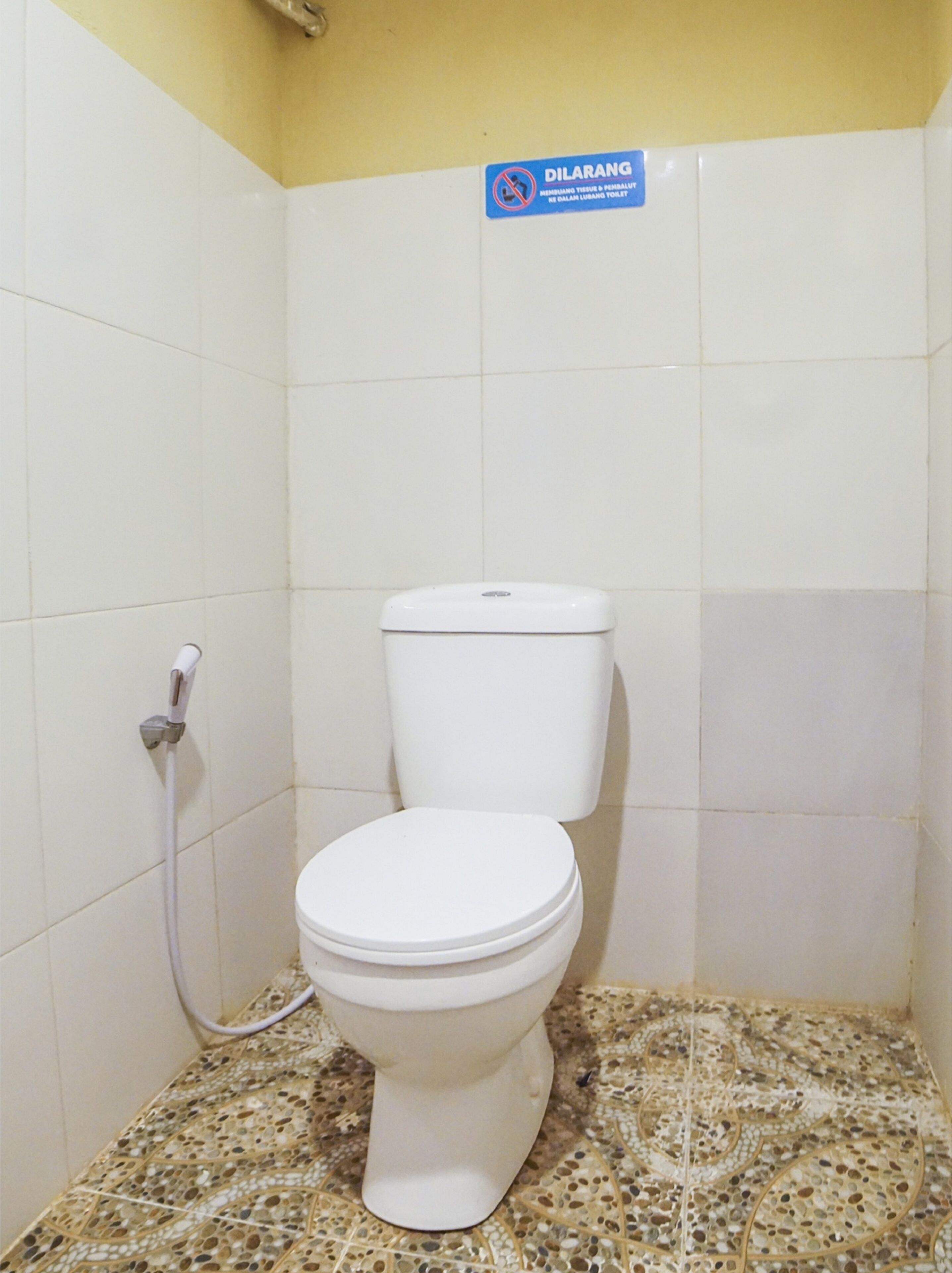 A toilet with a white seat and tank, a wall-mounted flush handle, and a sign above indicating a no-smoking policy.