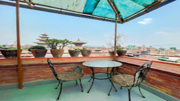 A balcony with a round table and two chairs, potted plants, and a view of traditional pagoda-style buildings in the distance. - MeroStay 222 Guest House DD (Bhaktapur)