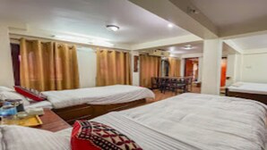A hotel room with two beds, a desk with a chair, and a small table with a red cushion. - MeroStay 222 Guest House DD (Bhaktapur)