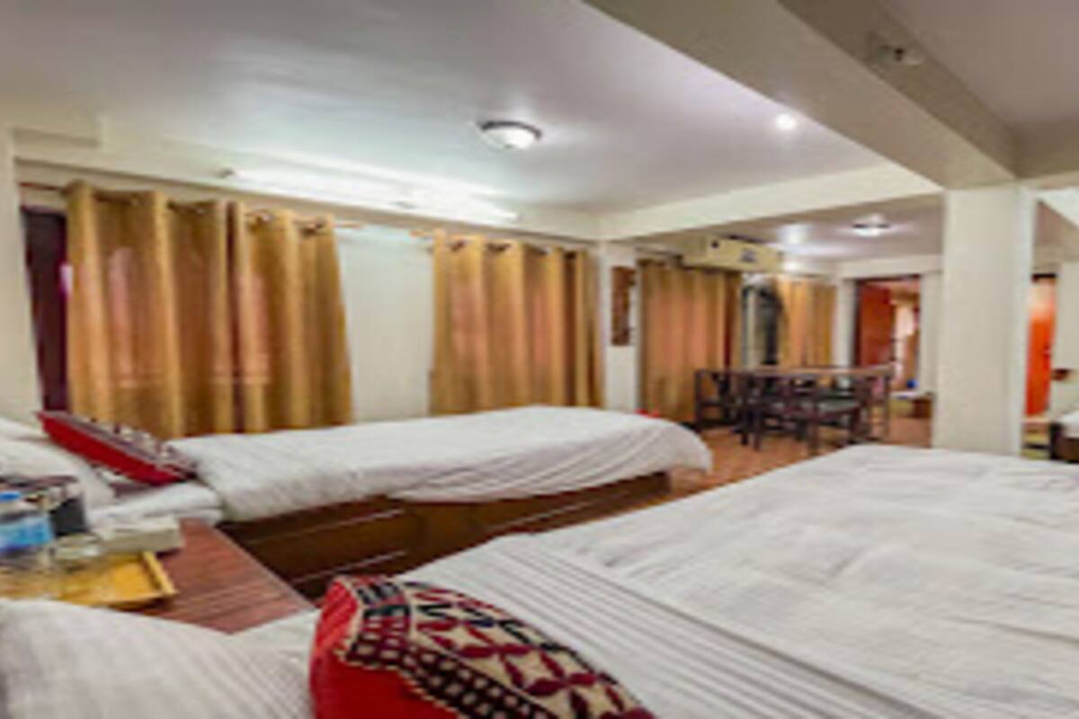Une chambre d’hôtel avec deux lits, un bureau avec une chaise et une petite table surmontée d’un coussin rouge.
