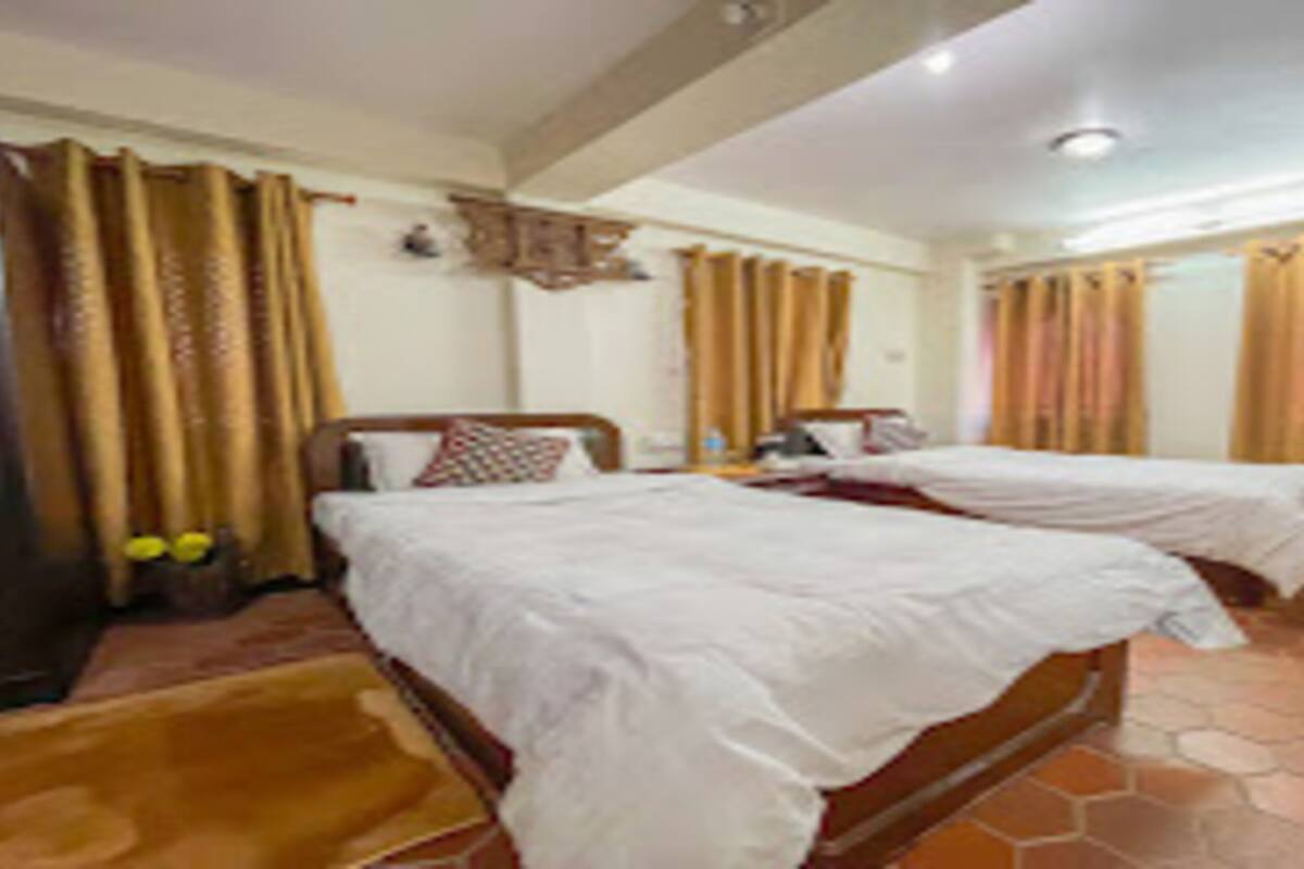 Une chambre d’hôtel avec deux lits, une tête de lit en bois, une petite table avec une lampe et une fenêtre avec des rideaux.