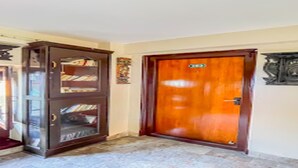 A wooden door with a brass handle, a glass-fronted cabinet with books, and a wall-mounted clock. - MeroStay 222 Guest House DD (Bhaktapur)