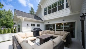 Une terrasse couverte avec un canapé d’angle, une table et un barbecue.