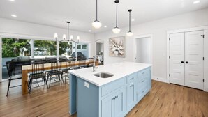 Une cuisine spacieuse dotée d’un grand îlot central, de planchers en bois et de luminaires suspendus.