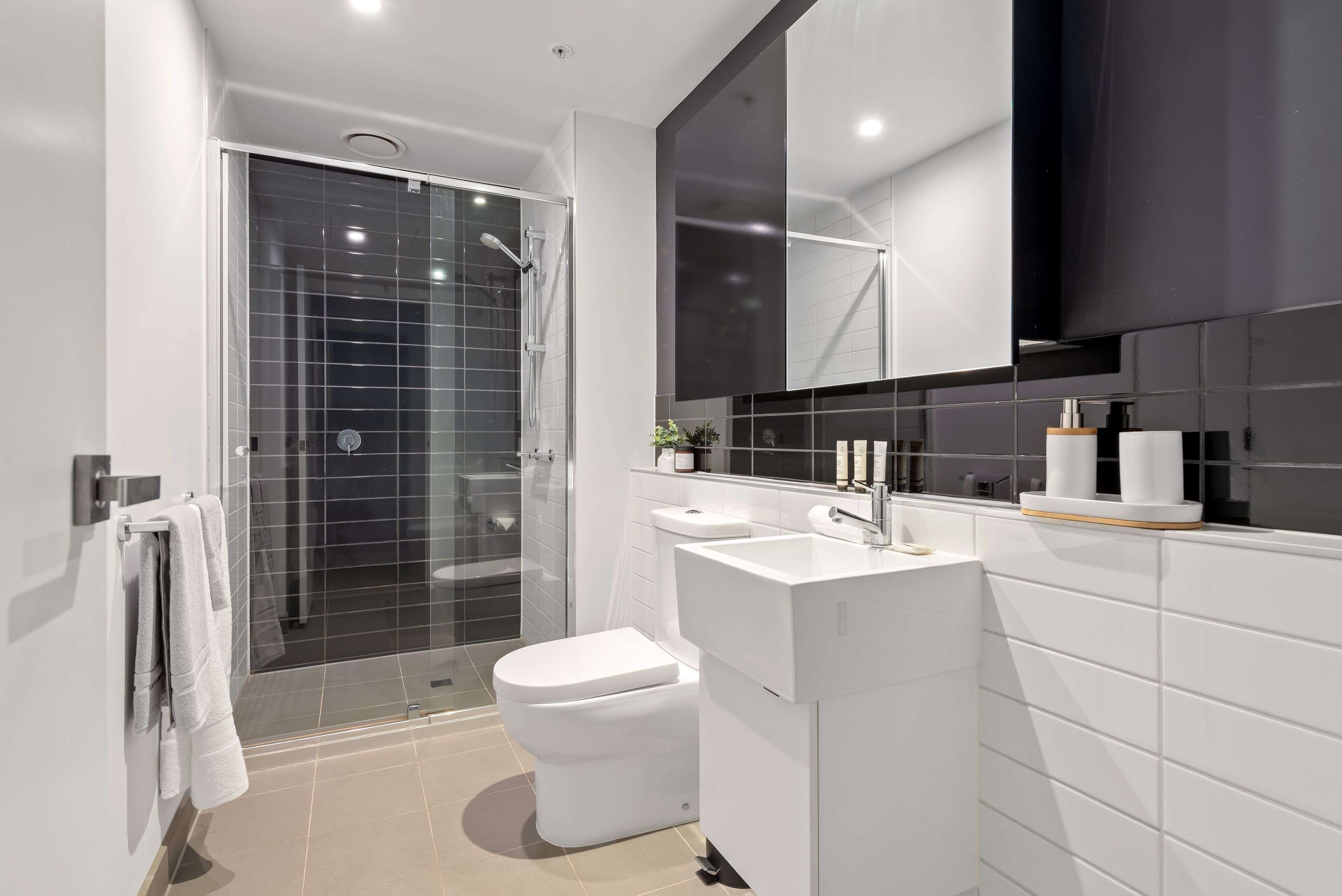 A modern bathroom with a glass-enclosed shower, a white toilet, and a sink with a mirror above.