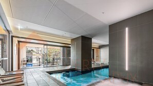 A modern indoor swimming pool with a clear view of the outside, a seating area with chairs, and a large glass door leading outside. - Simply Melbourne by Ready Set Stay - City Views, WIFI, full linen (Melbourne)