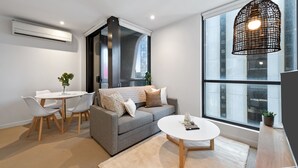 A modern living room with a grey sofa, white coffee table, and a large window with a view of the city. - Simply Melbourne by Ready Set Stay - City Views, WIFI, full linen (Melbourne)