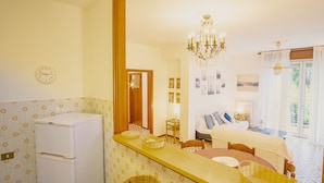 Une chambre d’hôtel avec un lit, une table à manger, un lustre, un réfrigérateur et une horloge murale.
