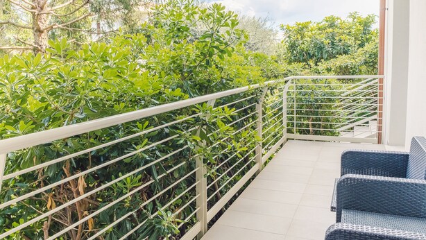 Un balcon avec une rambarde en métal, un sol carrelé et une chaise en osier.