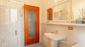 Une salle de bain Ă©quipĂ©e dâune douche, dâun lavabo, dâun miroir et dâune porte en bois avec un panneau de verre texturĂ©.