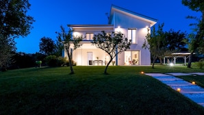 Ein modernes, zweigeschossiges Haus mit gepflegtem Rasen, einer Terrassenfläche und einem sichtbaren Sitzbereich im Freien.