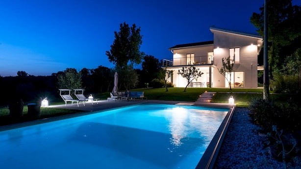 Ein modernes, zweistöckiges Haus mit Swimmingpool, Außenbereich zum Sitzen und gut beleuchteter Umgebung.