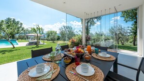 Ein Esstisch, gedeckt für ein Frühstück, mit Blick auf einen Swimmingpool und üppiges Grün.