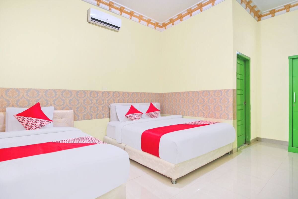 A hotel room with two beds, each with white bedding and red accents, a green door, and patterned wallpaper.