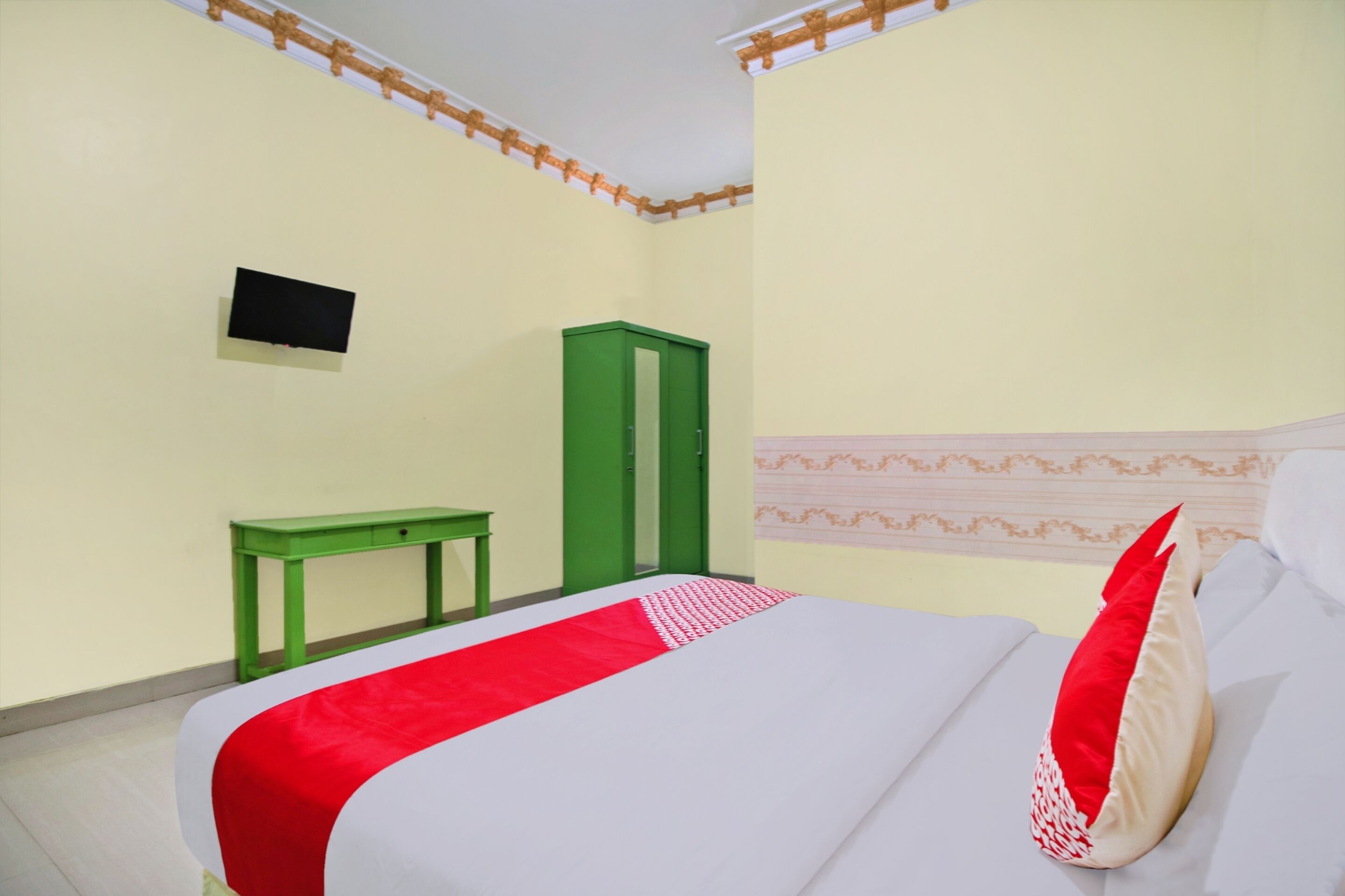 Ein Schlafzimmer mit einem Bett, einem grünen Wandschrank, einem kleinen Tisch und einem Fernseher an der Wand.