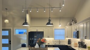 A modern kitchen with a large island, bar stools, pendant lighting, and a view of the living area.