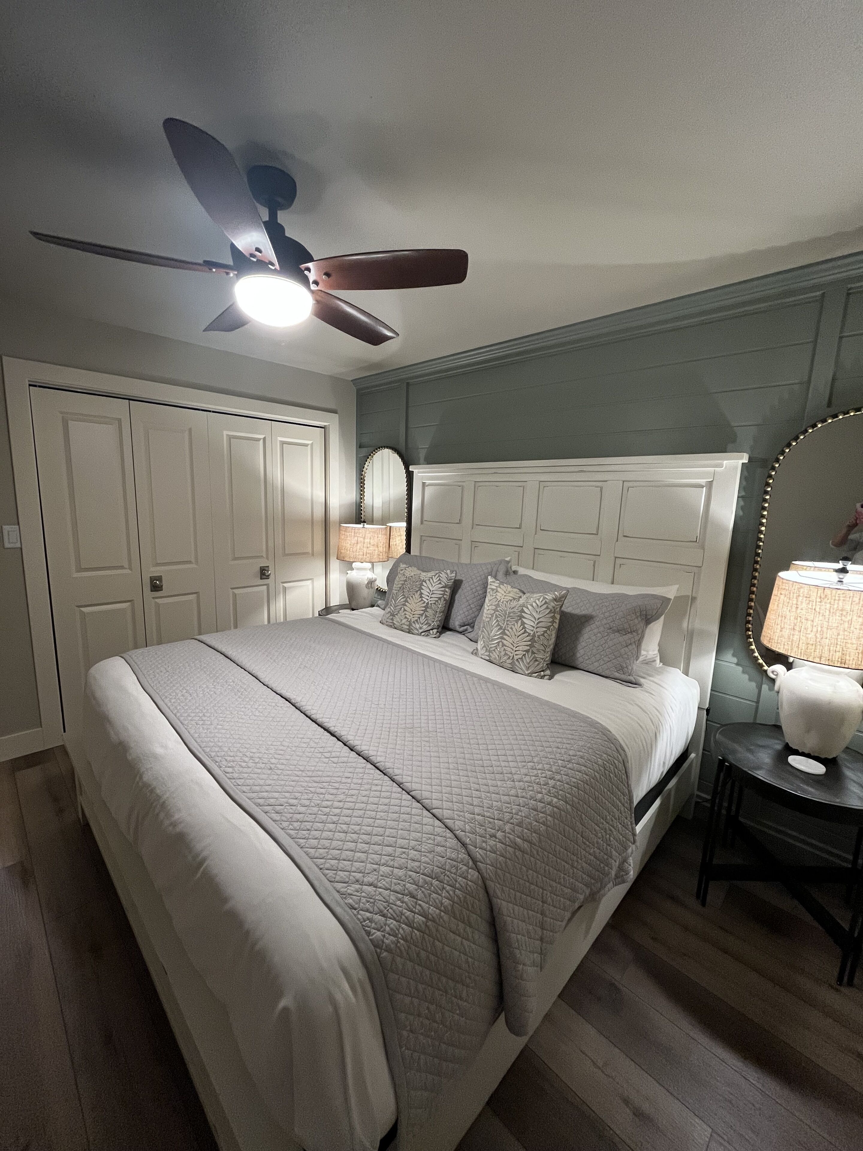 A bedroom with a bed, a ceiling fan, a nightstand with a lamp, and a dresser.