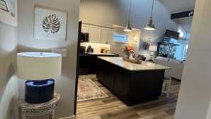 A modern kitchen with wooden flooring, a central island, pendant lighting, and a view into the dining area.