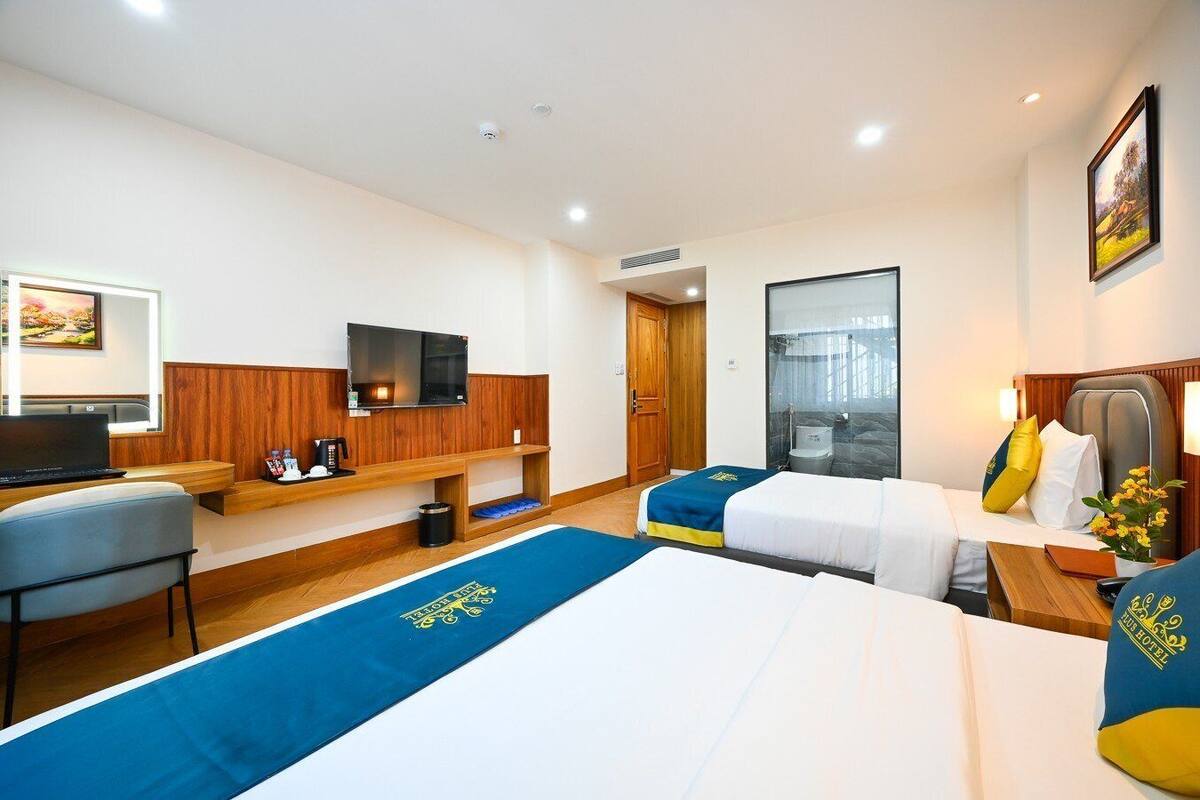 A hotel room with two beds, a desk with a laptop, a TV, and a shower area.
