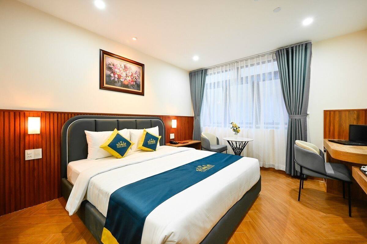 A hotel room with a bed, a desk, a chair, a small table, and a painting on the wall.