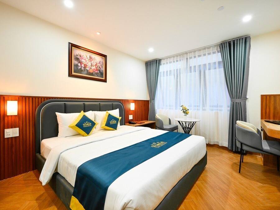 A hotel room with a bed, a desk, a chair, a small table, and a painting on the wall.