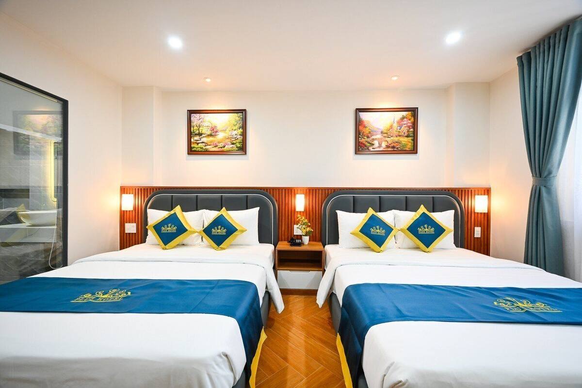 A hotel room with two beds, each with matching blue bedspreads and pillows, wooden headboards, and framed artwork on the walls.
