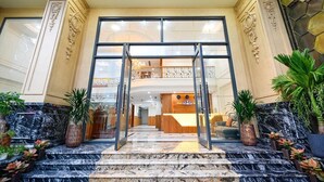 L’entrée d’un hôtel, avec un grand escalier, un comptoir d’accueil et un balcon agrémenté de balustrades décoratives.