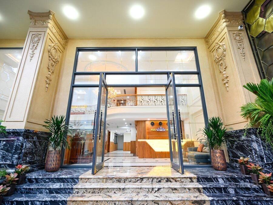 A hotel entrance with a grand staircase, a reception desk, and a balcony with decorative railings.