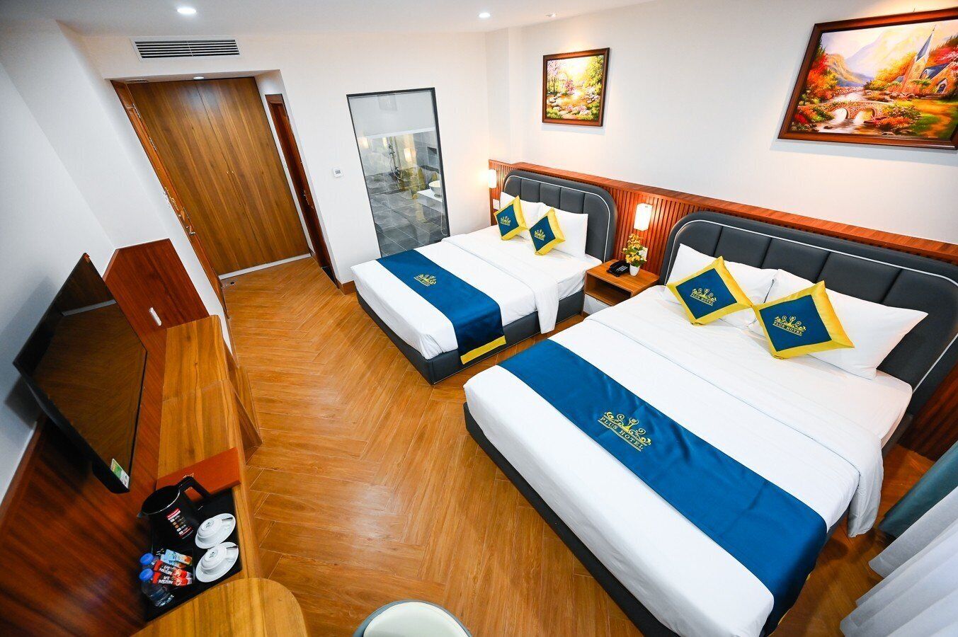 Une chambre d’hôtel avec deux lits, un plancher en bois, un bureau avec une chaise et une salle de bain visible à travers une porte en verre.