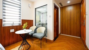 Une pièce avec un plancher en bois, une table ronde et deux chaises, une plante en pot et une porte coulissante donnant sur une salle de bain.