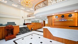 A hotel reception area with a marble floor, a wooden reception desk, a staircase, and a chandelier. - PLUS VUNG TAU HOTEL (Ho Chi Minh City)