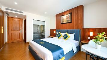 A hotel room with a large bed, wooden paneling on the walls, a painting above the bed, and a small table with a plant.