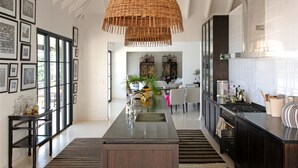 Una cocina moderna con una isla central, muebles negros y una lámpara colgante grande de fibras trenzadas.