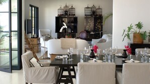 Una sala moderna con un sofá, una mesa de comedor dispuesta para seis personas y dos armarios negros con objetos decorativos.