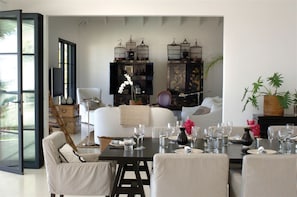 A modern living room with a sofa, dining table set for six, and two black cabinets with decorative items.
